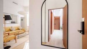 A modern living room with a sofa, a coffee table, and a large mirror reflecting a hallway. - 🌙 Lunero: Elegant One-Bedroom Retreat in Seville’s Historic Old Town (Sevilla)