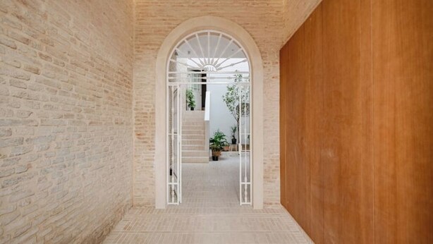 A hallway with brick walls, a wooden panel, and a white archway leading to a staircase. - 🌙 Lunero: Elegant One-Bedroom Retreat in Seville’s Historic Old Town (Sevilla)