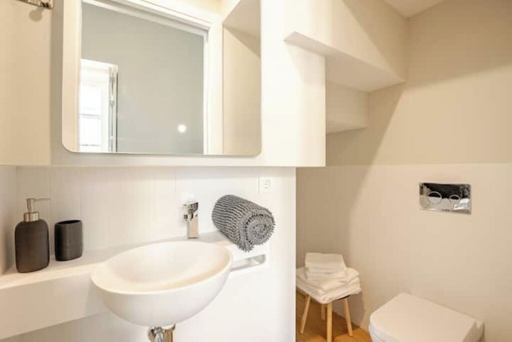 A bathroom with a white sink, a mirror above it, a towel rack, and a toilet.