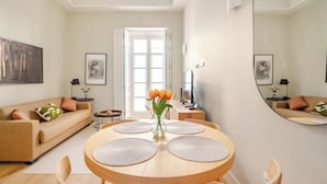 Uma sala de estar moderna com uma mesa de jantar redonda de madeira, um sofá bege e um espelho grande na parede.