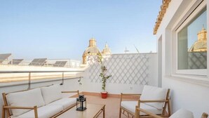 Terraço no telhado com sofá branco, mesa de madeira e planta em vaso.