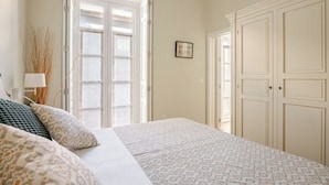 Quarto com cama, mesa de cabeceira, abajur e janela com vista para o exterior.