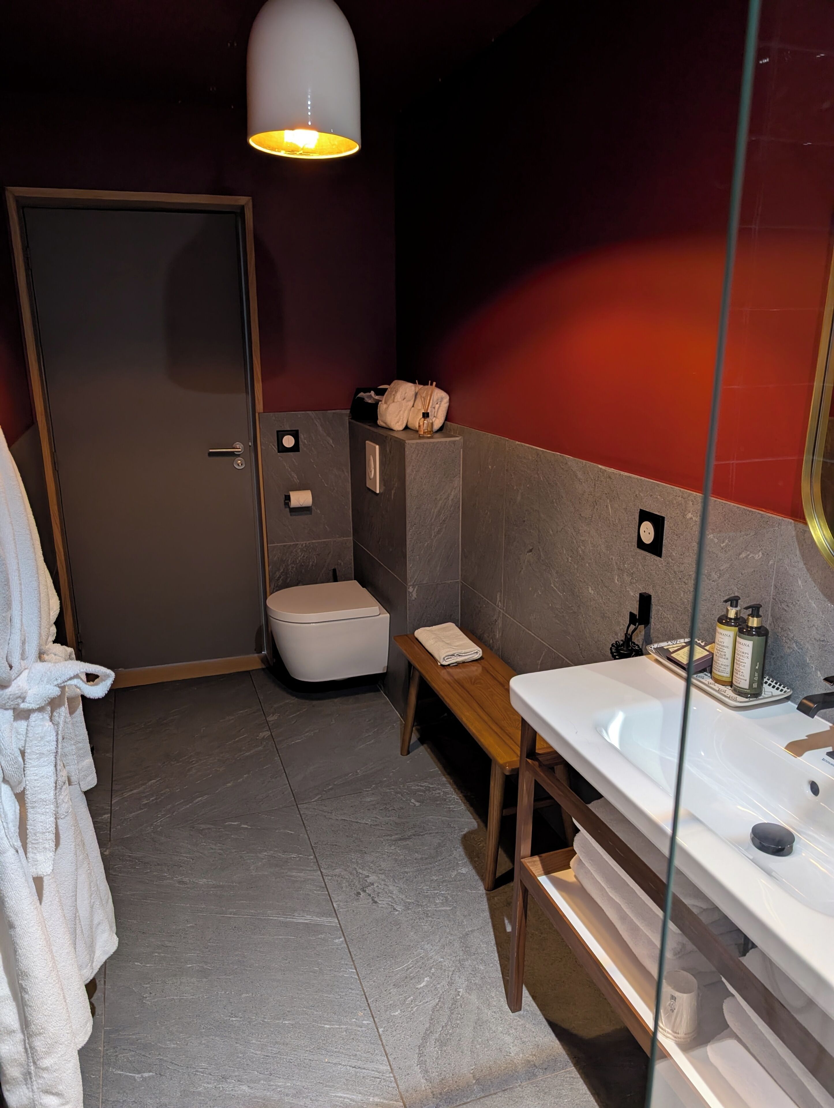 A modern bathroom with a white sink, a mirror, a bench, and a toilet.