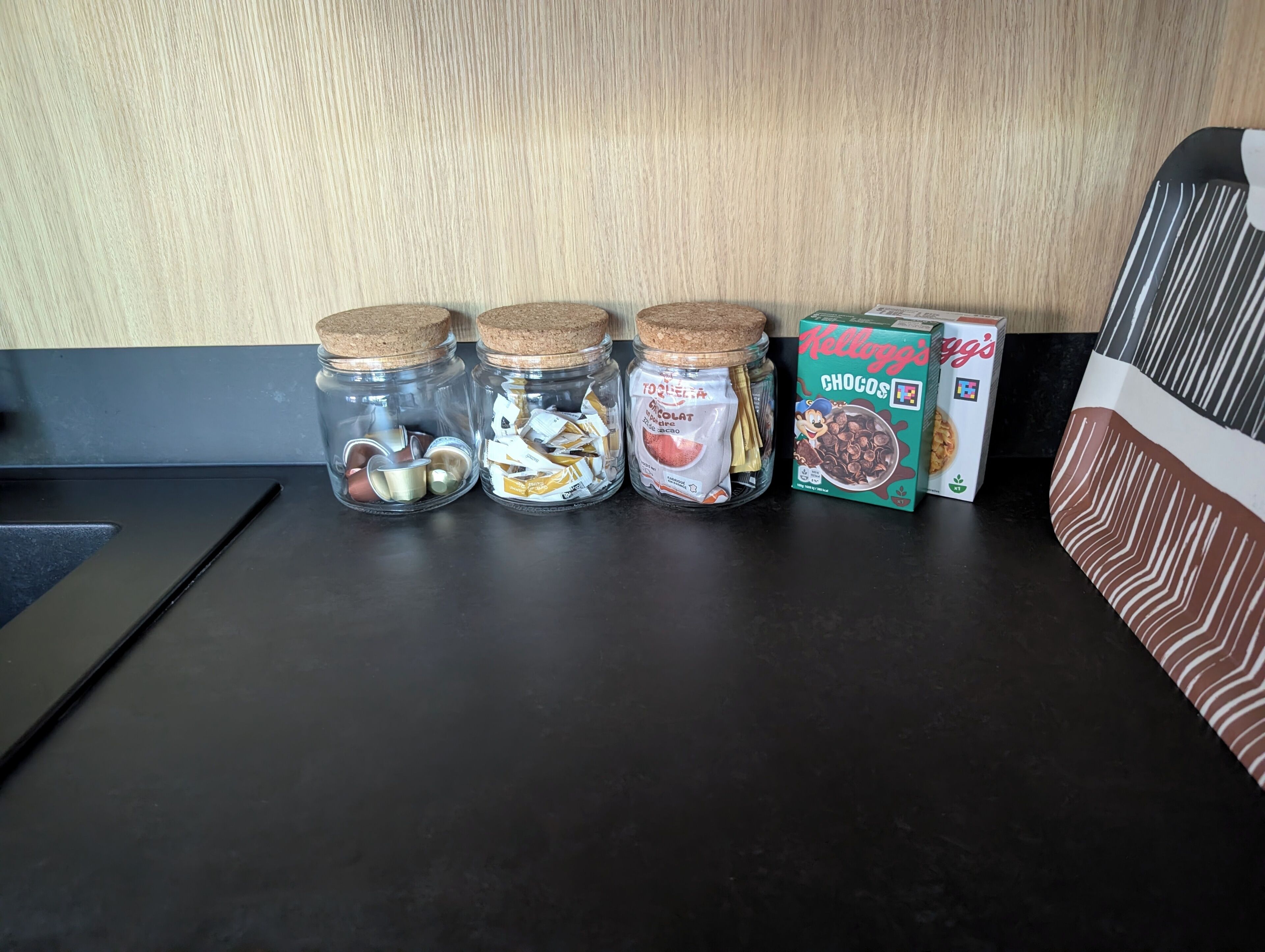 Vier glazen potten met kurken deksels, gevuld met verschillende objecten, op een donker aanrecht.