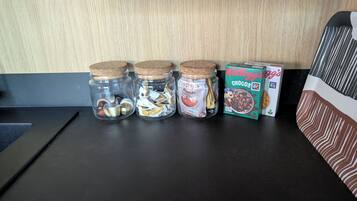 Vier glazen potten met kurken deksels, gevuld met verschillende objecten, op een donker aanrecht.