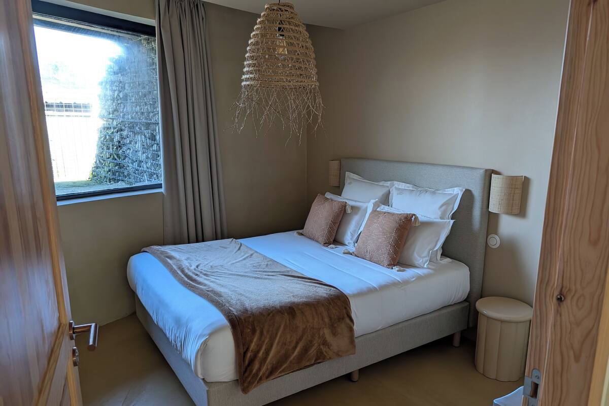 Un dormitorio con cama, mesitas de noche, lámpara colgante y ventana con cortinas.
