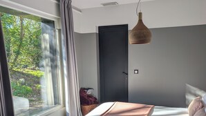 Een moderne slaapkamer met een groot bed, een raam met gordijnen, een deur en een hanglamp.