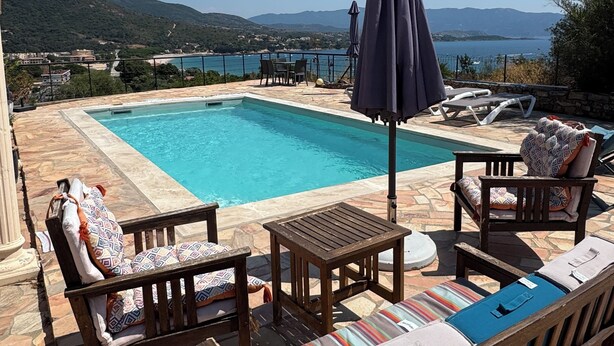 Un espace aménagé au bord de la piscine, offrant une vue sur la mer et les montagnes.