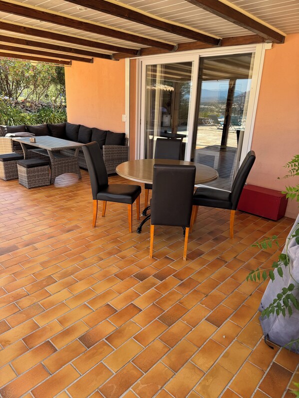 An outdoor patio with a round table and chairs, a sofa, and a glass door leading to a deck.