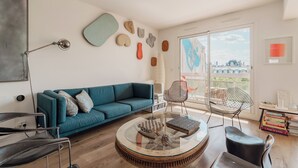 Un soggiorno moderno con un divano color acquamarina, un tavolino da caffè rotondo in vetro e vista sulla città attraverso ampie finestre.