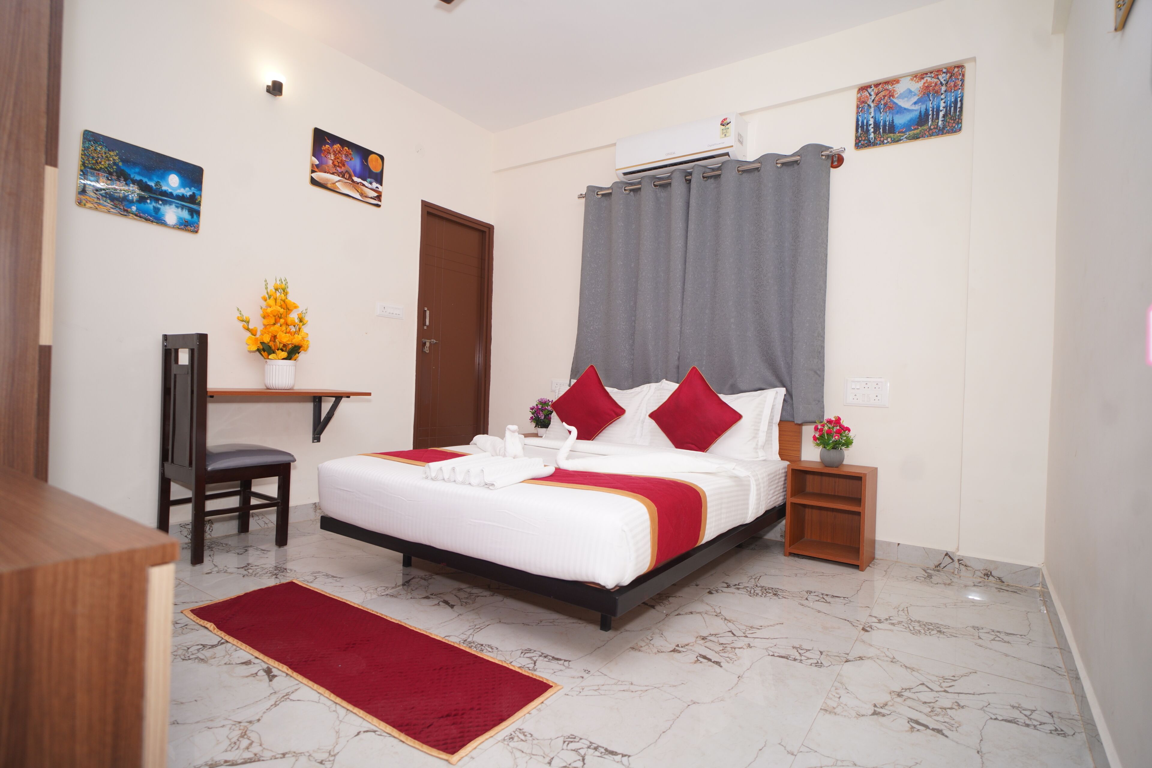 Una habitación de hotel con cama, escritorio, silla, alfombra roja y obras de arte en las paredes.