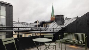 A rooftop terrace with a green bench, a small table, and a view of a church spire. - The Grand Residence is a luxurious four-bedroom suite in the heart of Stockholm (Stockholms län)