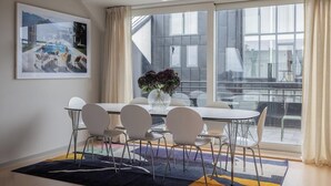A modern dining area with a large window, a dining table with chairs, and a vase with flowers. - The Grand Residence is a luxurious four-bedroom suite in the heart of Stockholm (Stockholms län)
