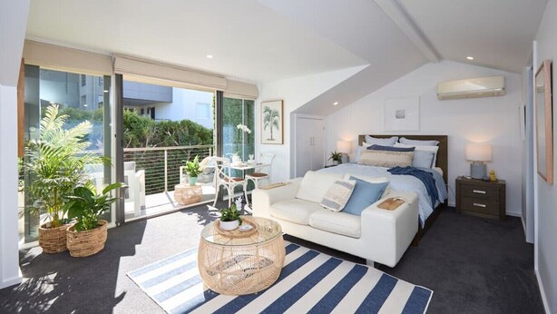 Une chambre moderne avec un grand lit, un balcon agrémenté de plantes en pot et une vue sur la ville.