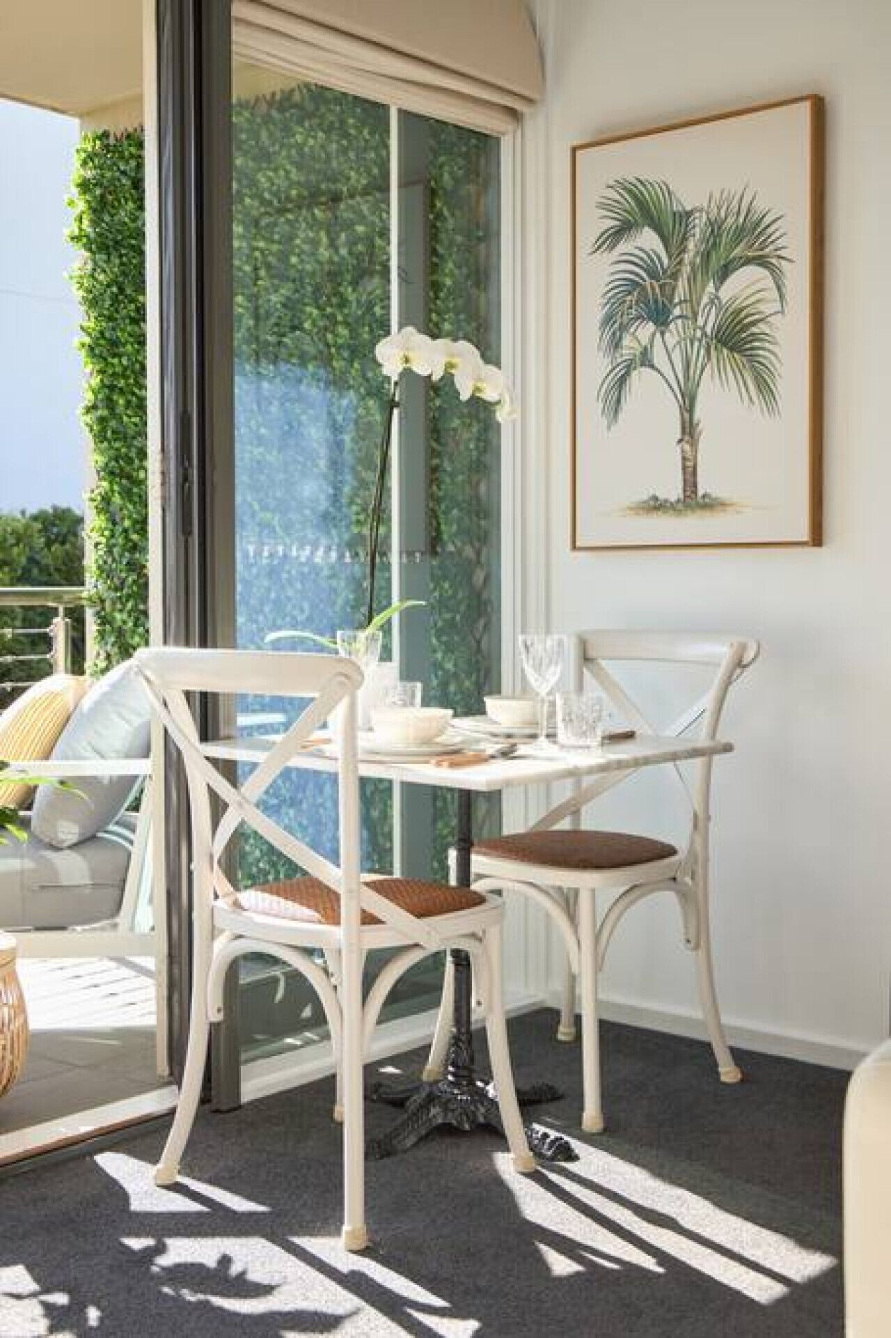 Un balcon avec une table et des chaises blanches, une plante en pot et une vue sur la verdure.