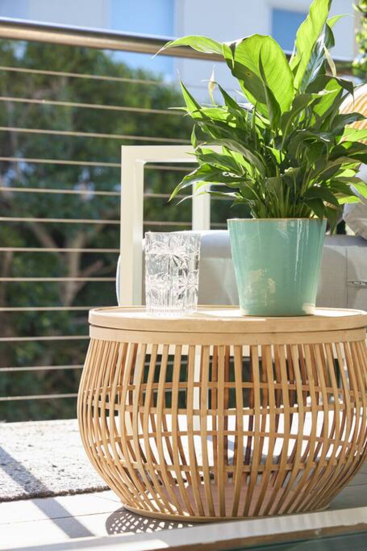 A wicker table with a potted plant and a glass on a balcony.