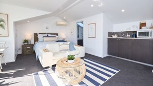 Une chambre moderne et bien éclairée, dotée d’un grand lit, de tables de chevet et offrant une vue sur la cuisine.