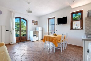 Ein Essbereich mit Tisch, Stühlen, einem weißen Kühlschrank, einem an der Wand montierten Fernseher und einem Fenster mit Blick auf Grünflächen.