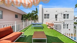 A rooftop terrace with artificial grass, outdoor furniture, and a striped canopy. - Blue Flamingo Suites (Miami Beach)