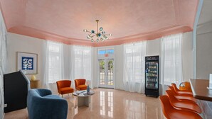 A hotel lobby with a pink ceiling, a modern chandelier, a vending machine, and orange and blue seating. - Blue Flamingo Suites (Miami Beach)