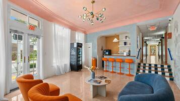 Un vestíbulo con asientos naranja y azul, una máquina expendedora y una escalera que lleva a otra zona.