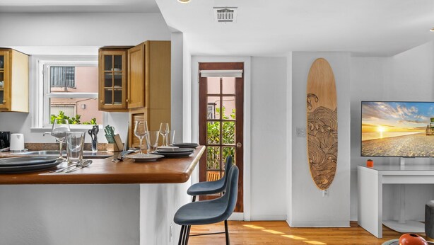 A modern kitchen with wooden cabinets, a dining area with a bar, and a surfboard decoration. - Blue Flamingo Suites (Miami Beach)