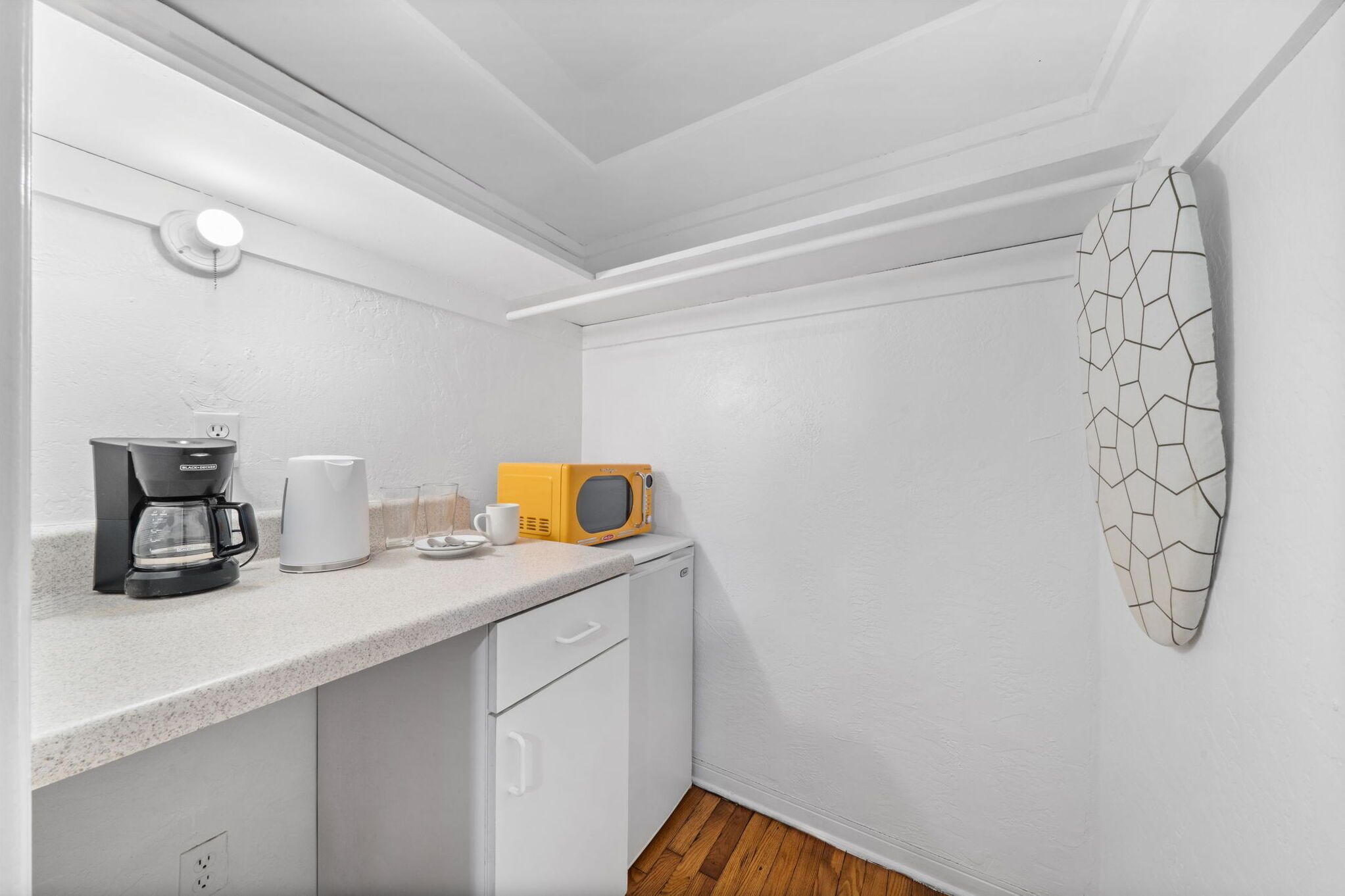 Cozinha compacta com armários brancos, cafeteira, micro-ondas e um objeto decorativo na parede.