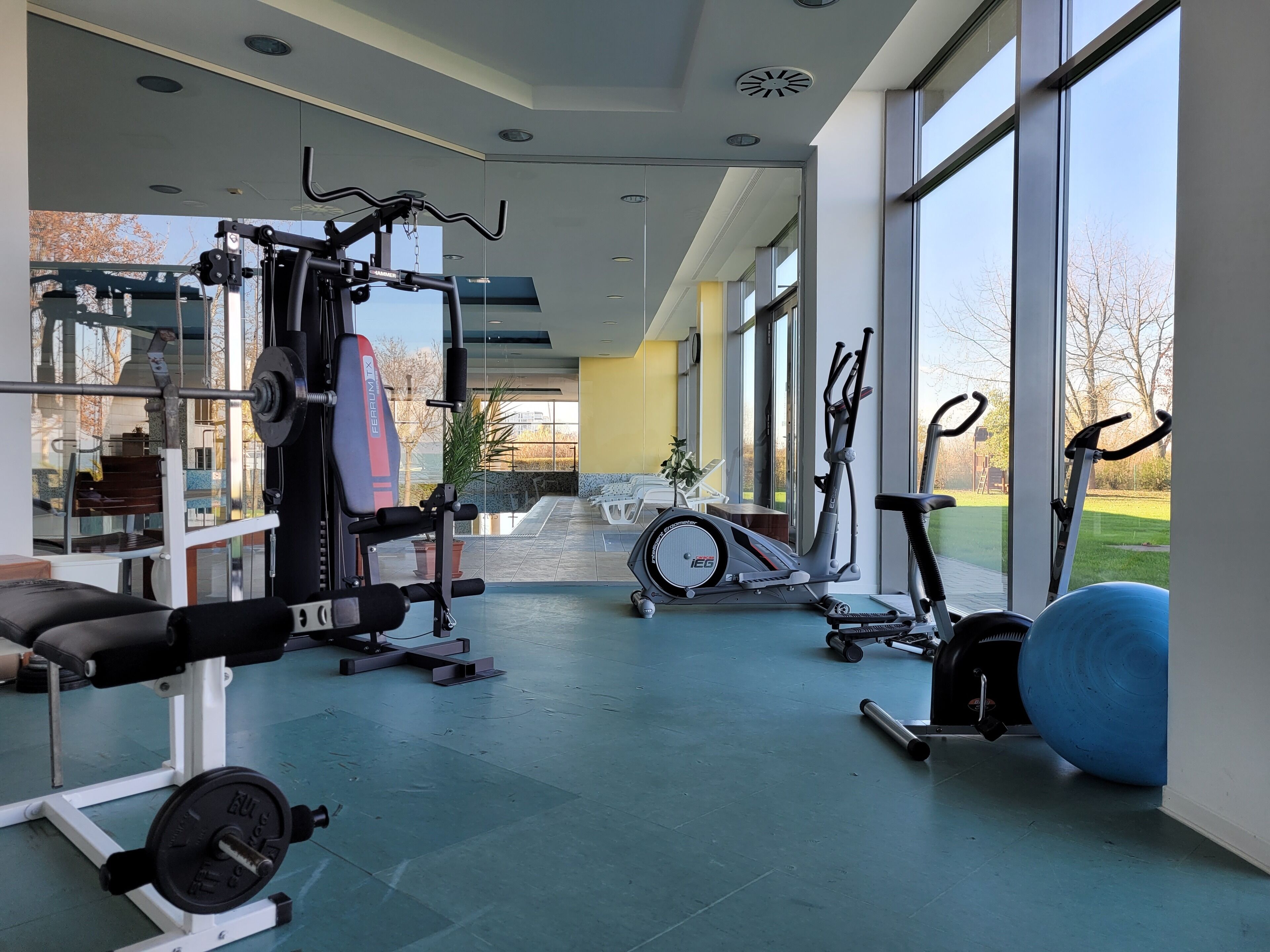 Un gimnasio con diverso equipo de ejercicio, incluyendo una banca, una banca de pesas, una elíptica y una bicicleta estática.