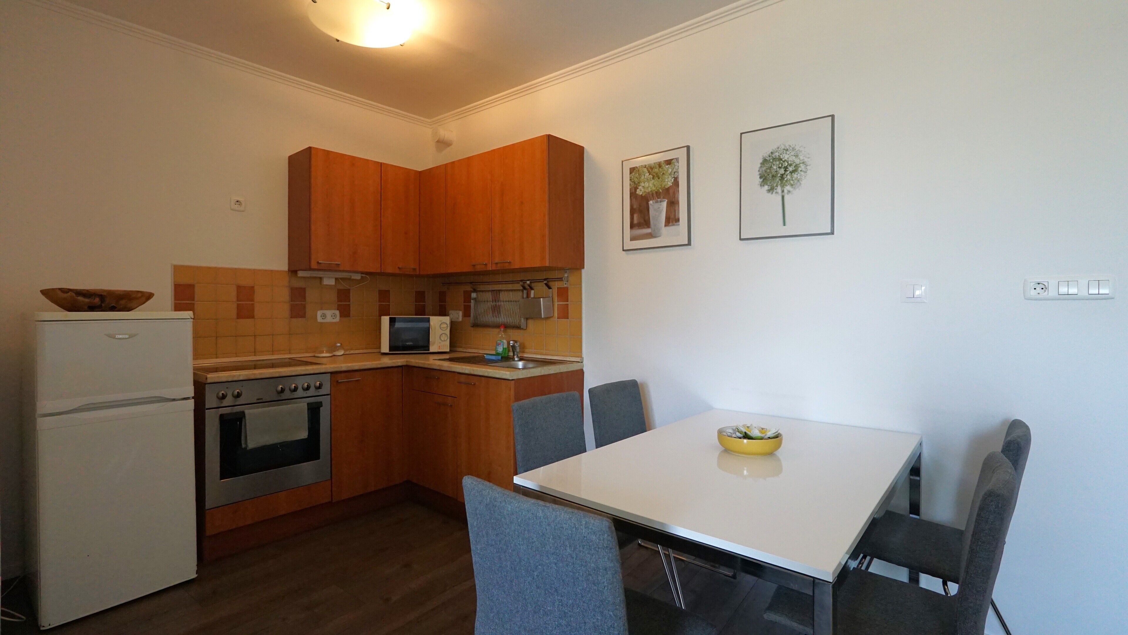 A compact kitchen with wooden cabinets, a microwave, a stove, and a dining table with chairs.