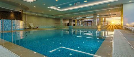 An indoor swimming pool with clear water, tiled walls, and a sunlit entrance.