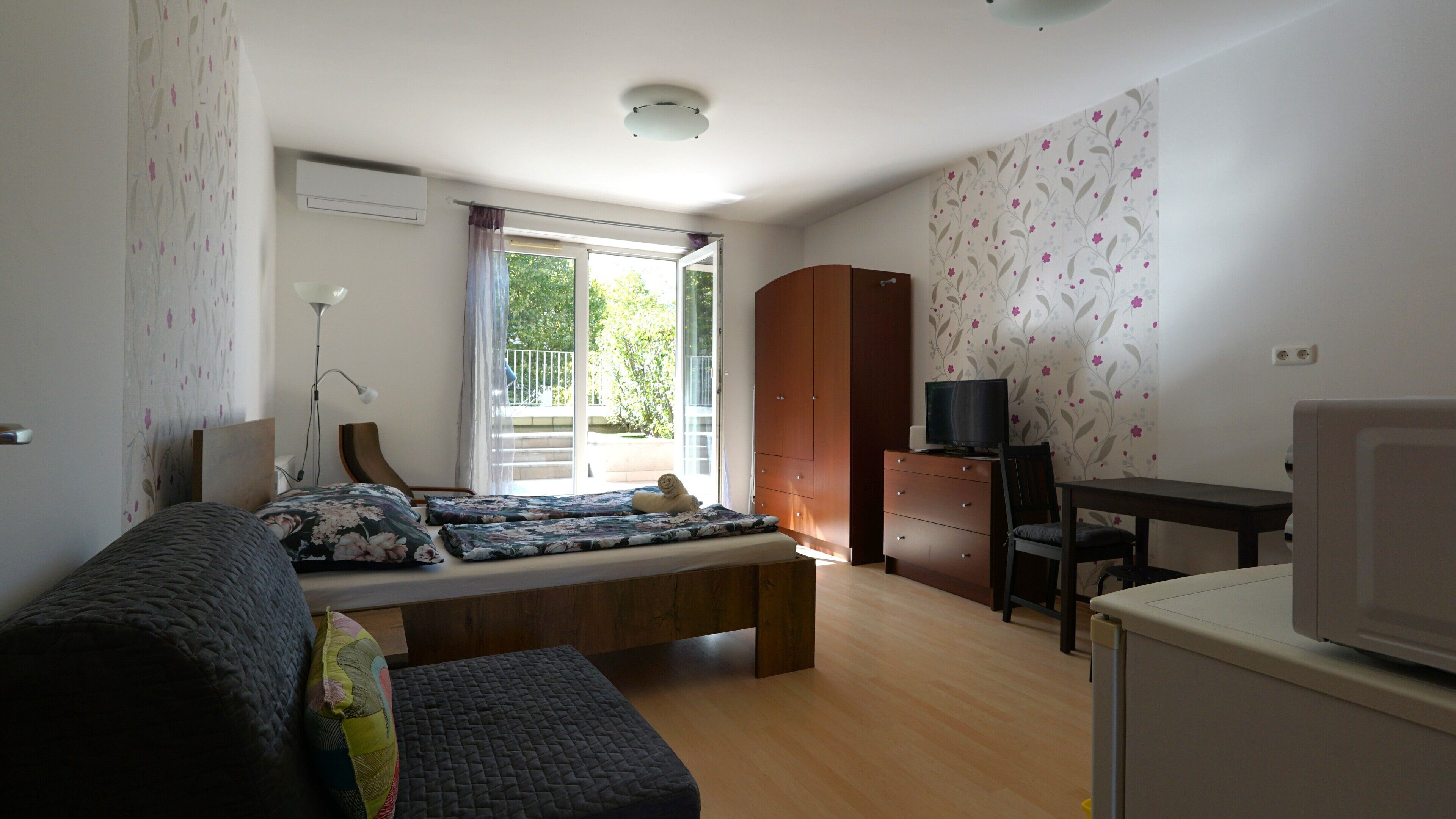 Een slaapkamer met een bed, een bureau, een televisie en een kledingkast.