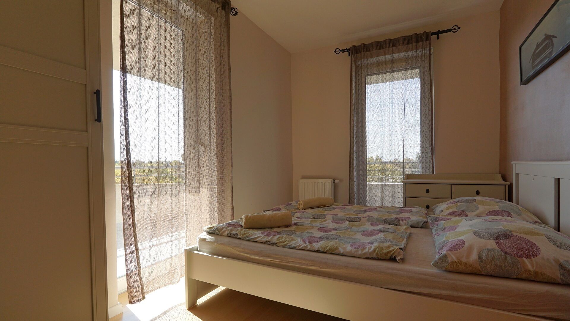 A bedroom with a bed, a dresser, a window with curtains, and a radiator.