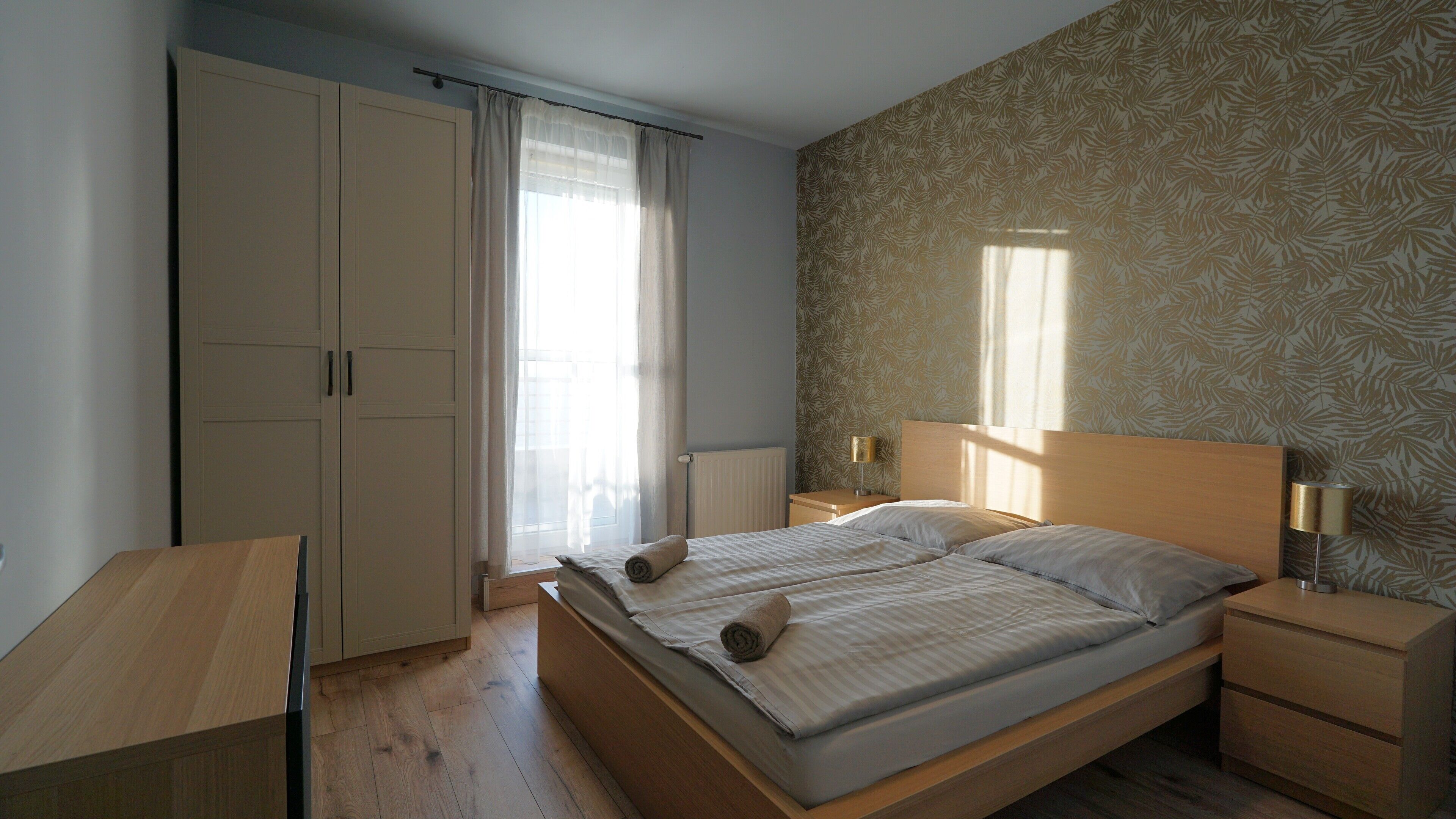 A bedroom with a bed, nightstands, a wardrobe, and a window with curtains.