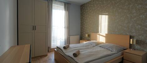 A bedroom with a bed, nightstands, a wardrobe, and a window with curtains.