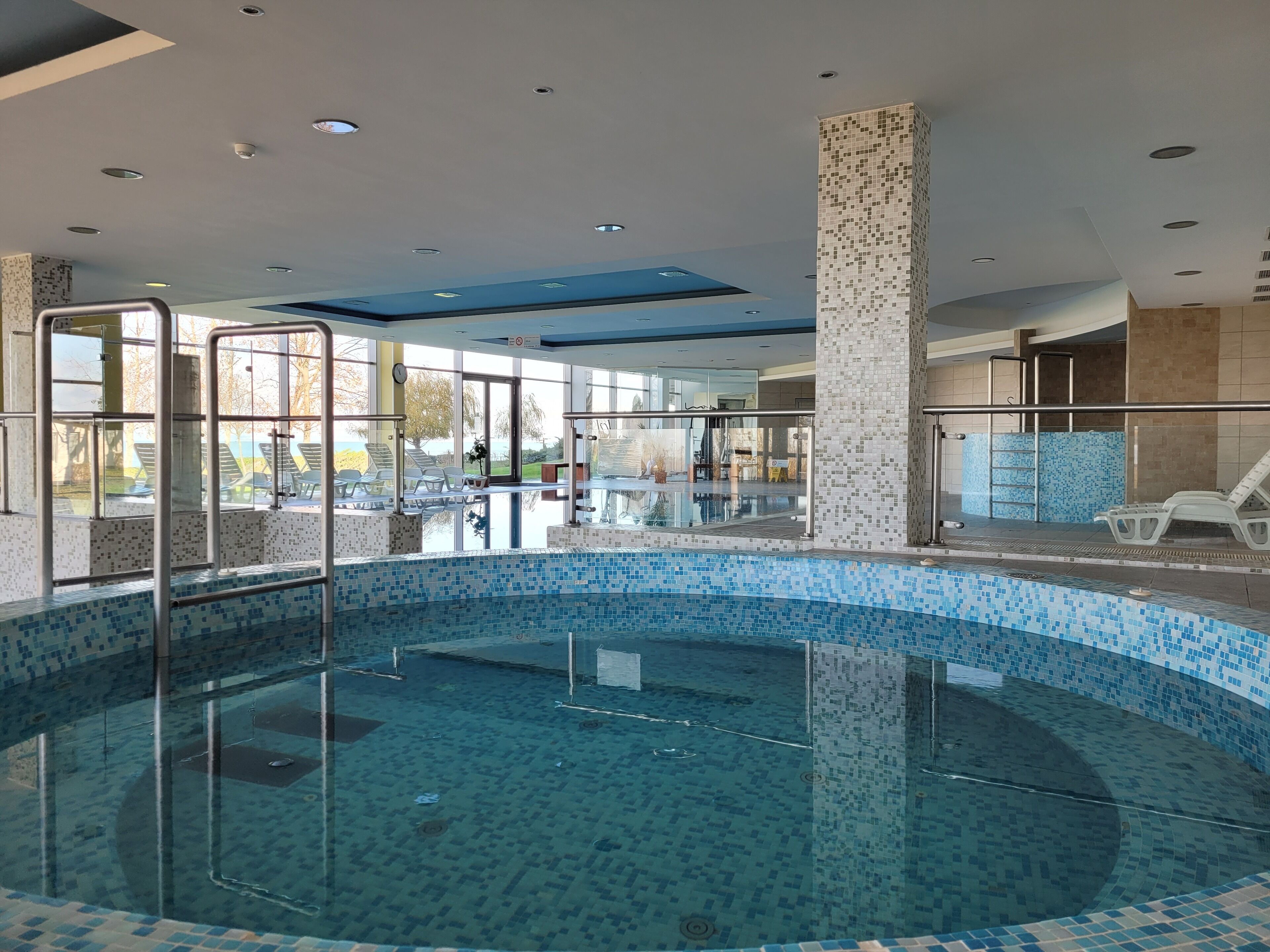 Una piscina interior con paredes de vidrio transparente, suelo de baldosas y vistas al exterior.