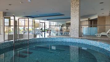 Una piscina interior con paredes de vidrio transparente, suelo de baldosas y vistas al exterior.