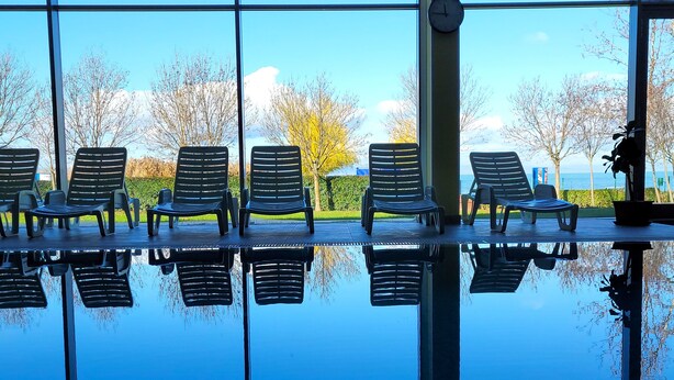 A row of lounge chairs with a view of trees and a clock on the wall. - Club218 Wellness Apartments (Siófok)