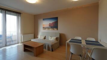 A modern room with a bed, a desk, and a chair. There is a window with curtains, a radiator, and a painting on the wall.