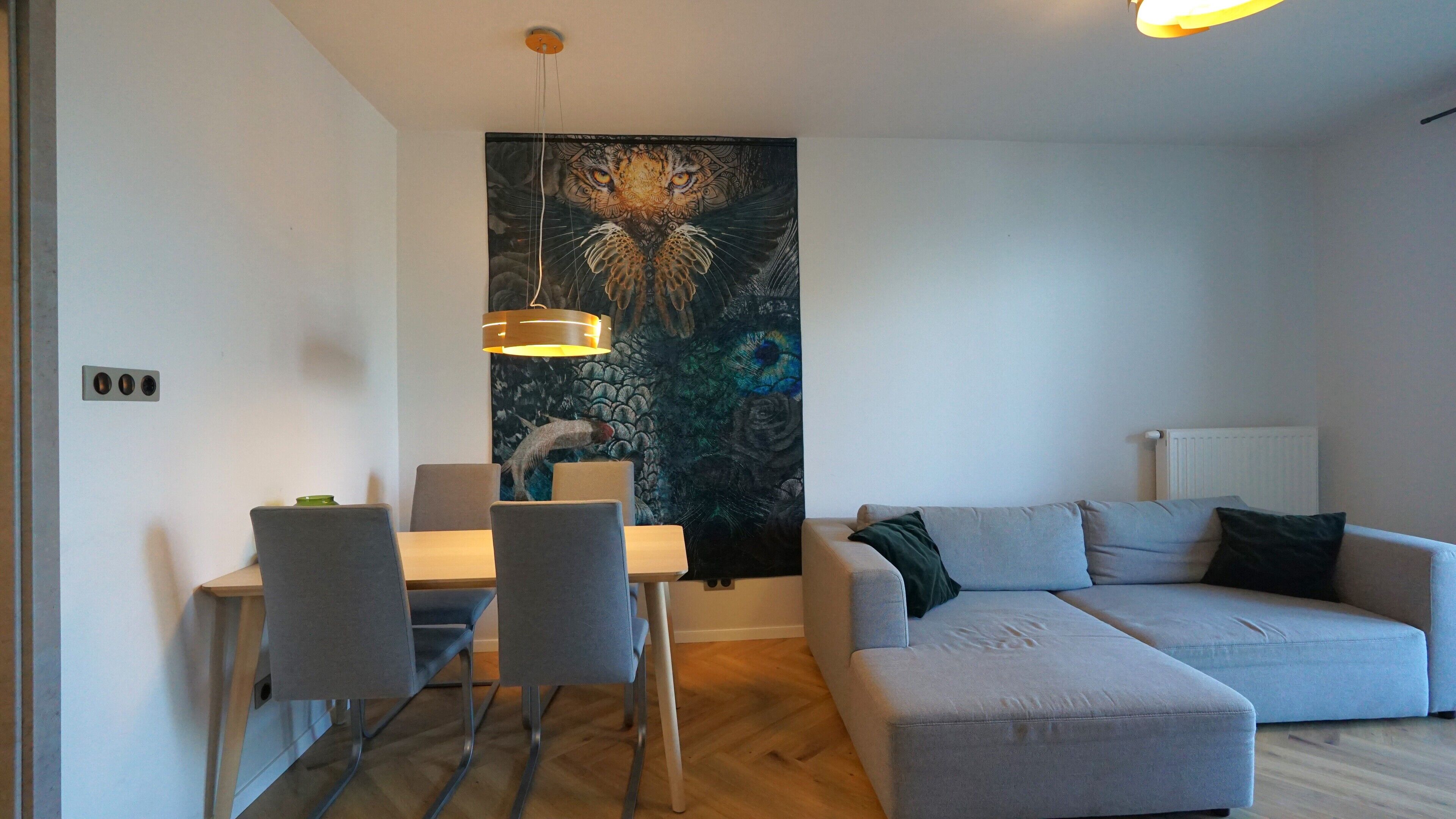Un salon moderne avec un canapé d’angle gris, une table à manger avec des chaises et un grand tableau abstrait accroché au mur.