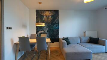 Un salon moderne avec un canapé d’angle gris, une table à manger avec des chaises et un grand tableau abstrait accroché au mur.