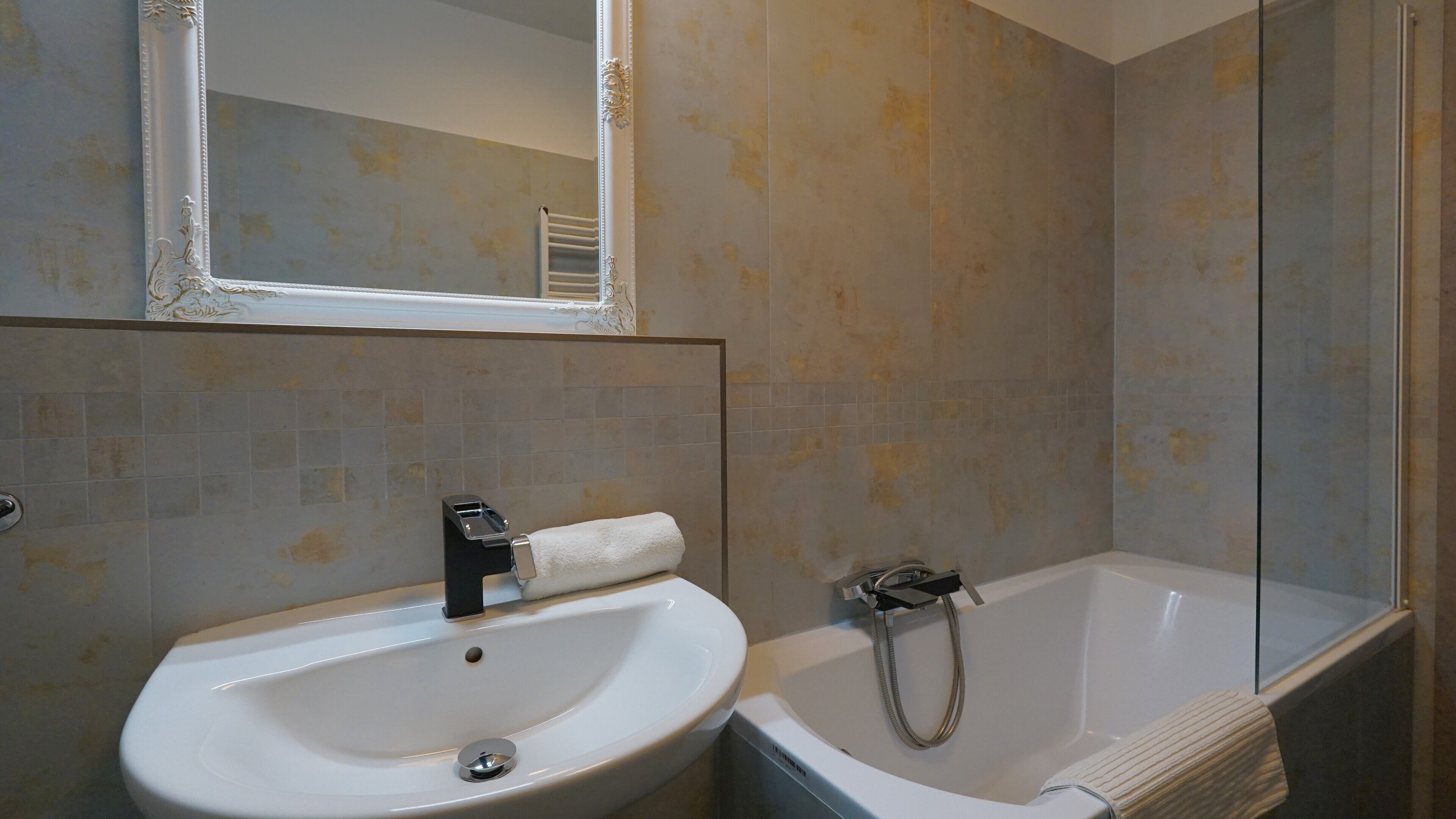 Un baño con lavamanos blanco, espejo y bañera.
