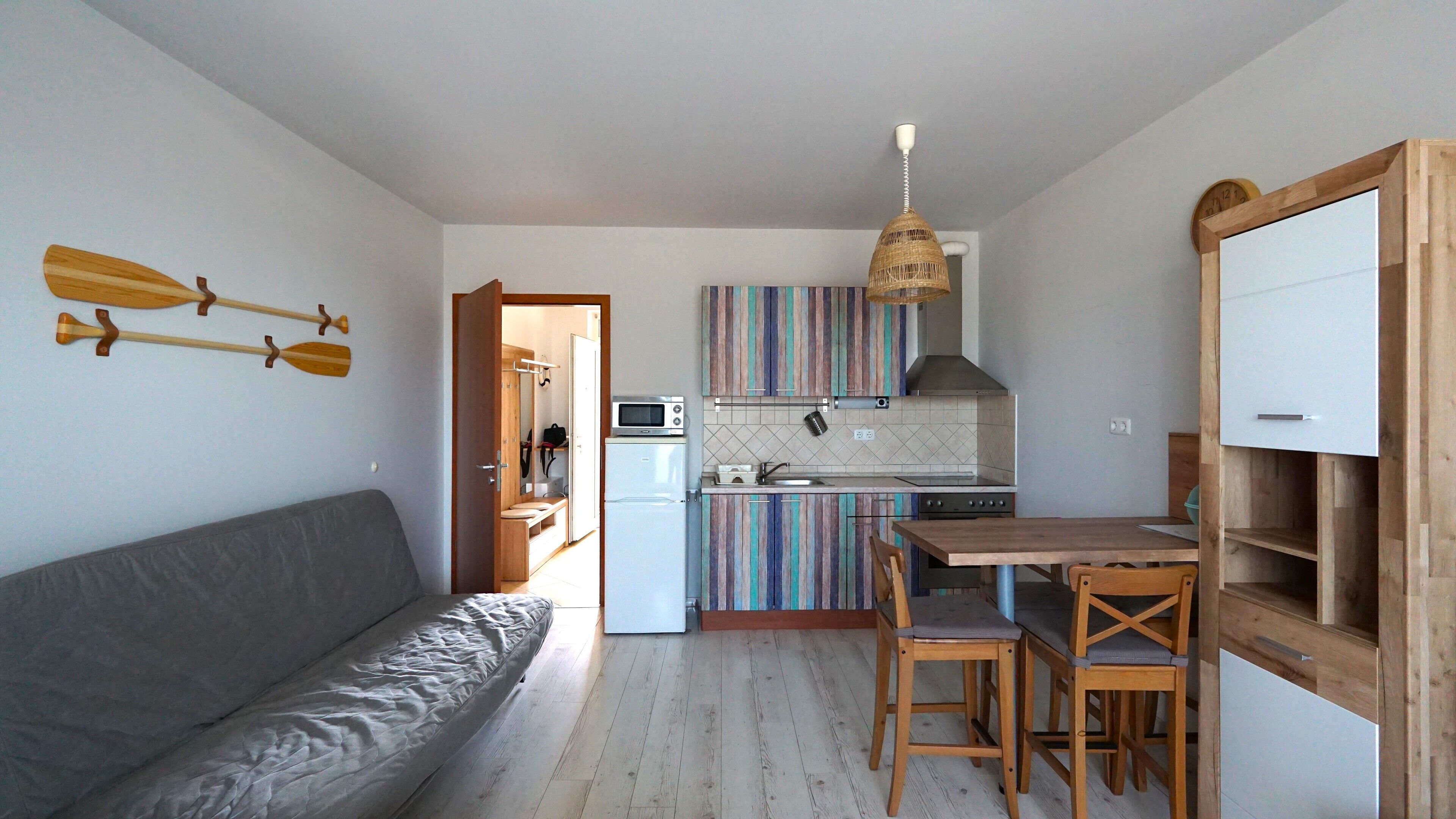 Eine kompakte Küche mit Mikrowelle, Toaster und Spüle. Im Wohnbereich steht ein Holzessttisch mit Stühlen und ein graues Sofa.