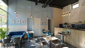 A modern cafe with a blue and white color scheme, featuring a bar area, seating with tables and chairs, and pendant lighting. - Club218 Wellness Apartments (Siófok)