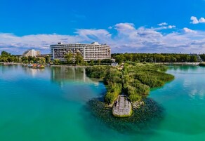 A waterfront hotel with a large building, a small island with vegetation, and clear blue water.