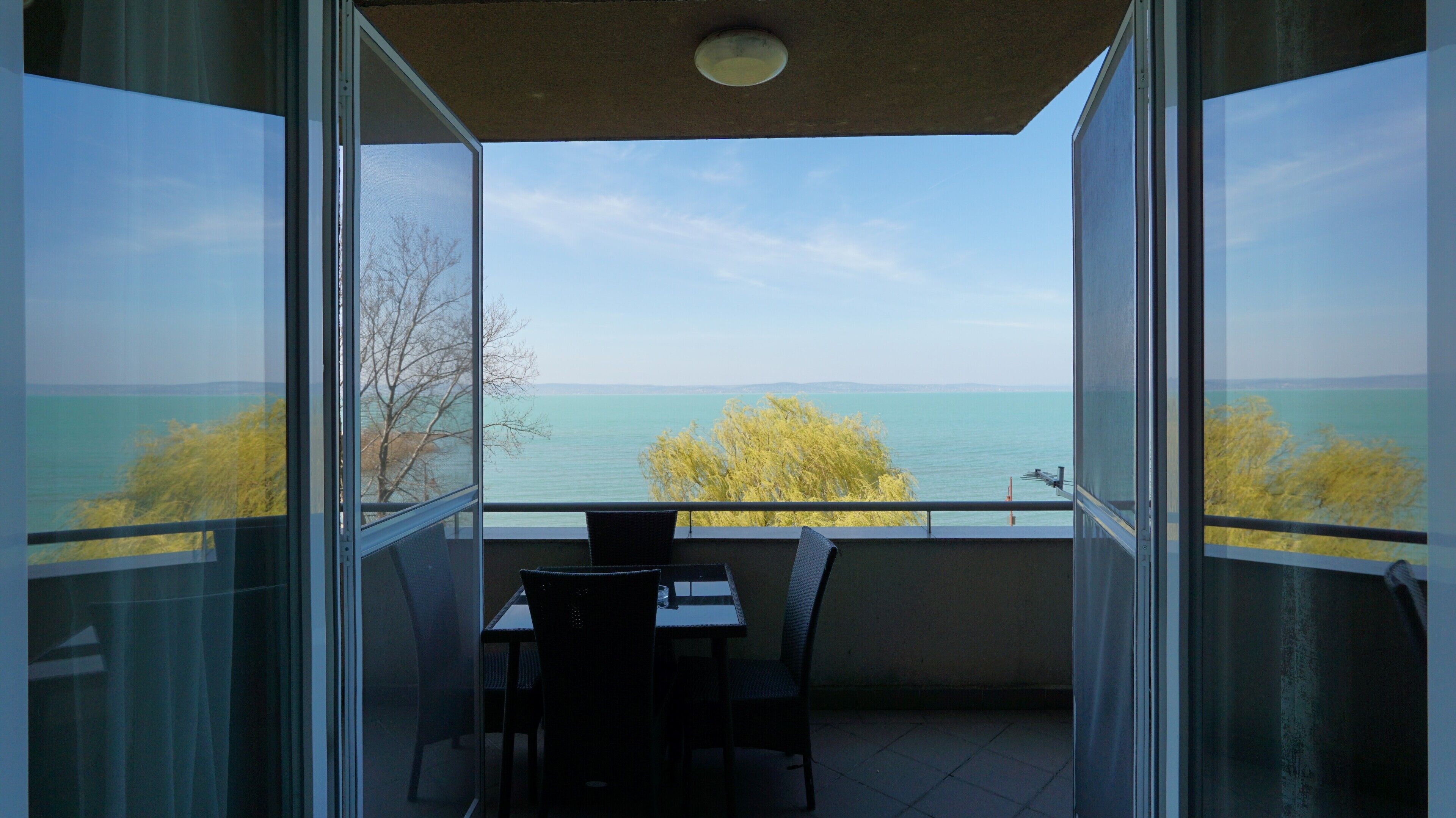 A balcony with a table and chairs, overlooking a body of water and trees.