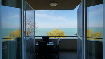 A balcony with a table and chairs, overlooking a body of water and trees.