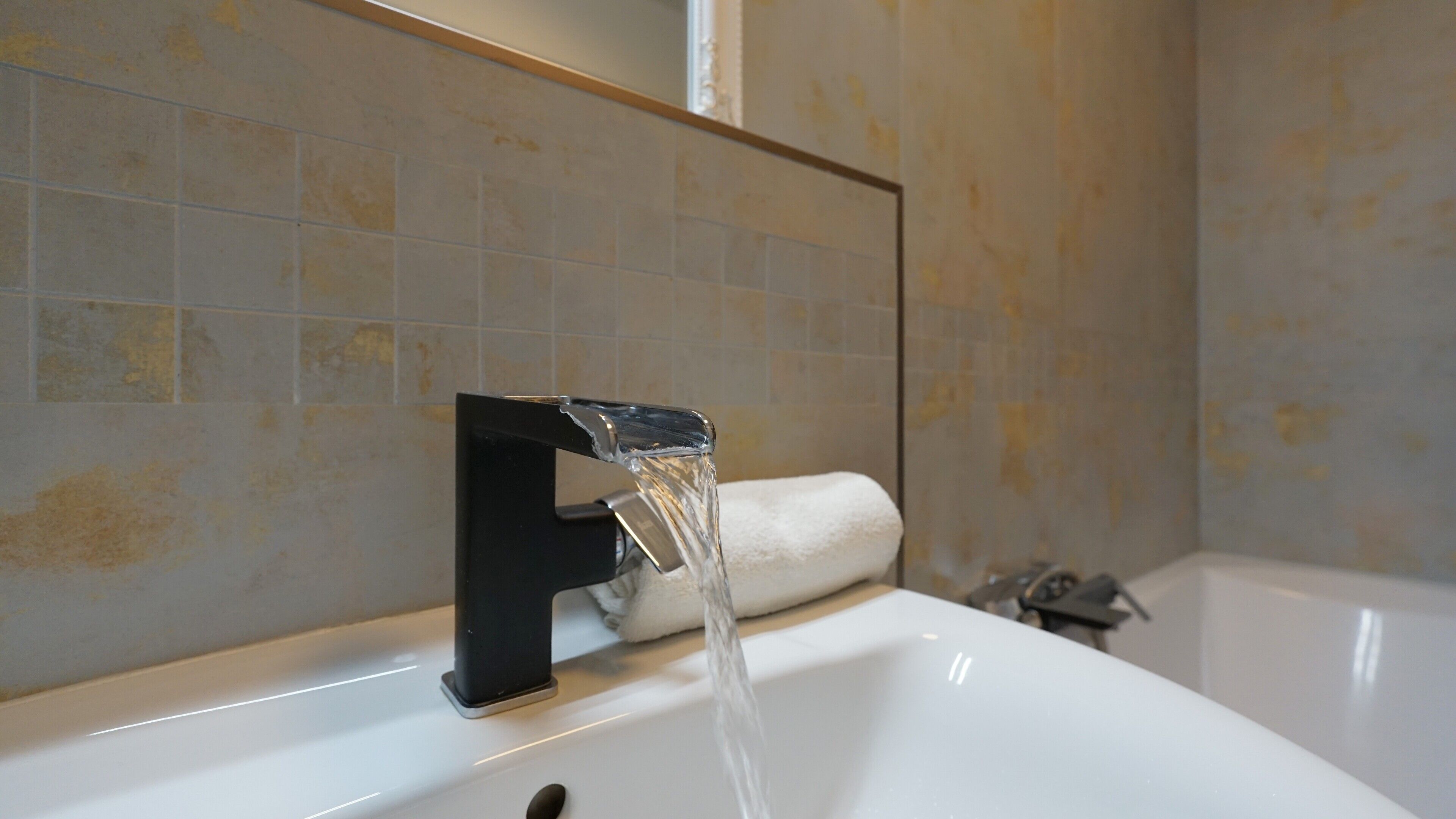 A bathroom with a sink, running water from a faucet, and a towel on the wall.