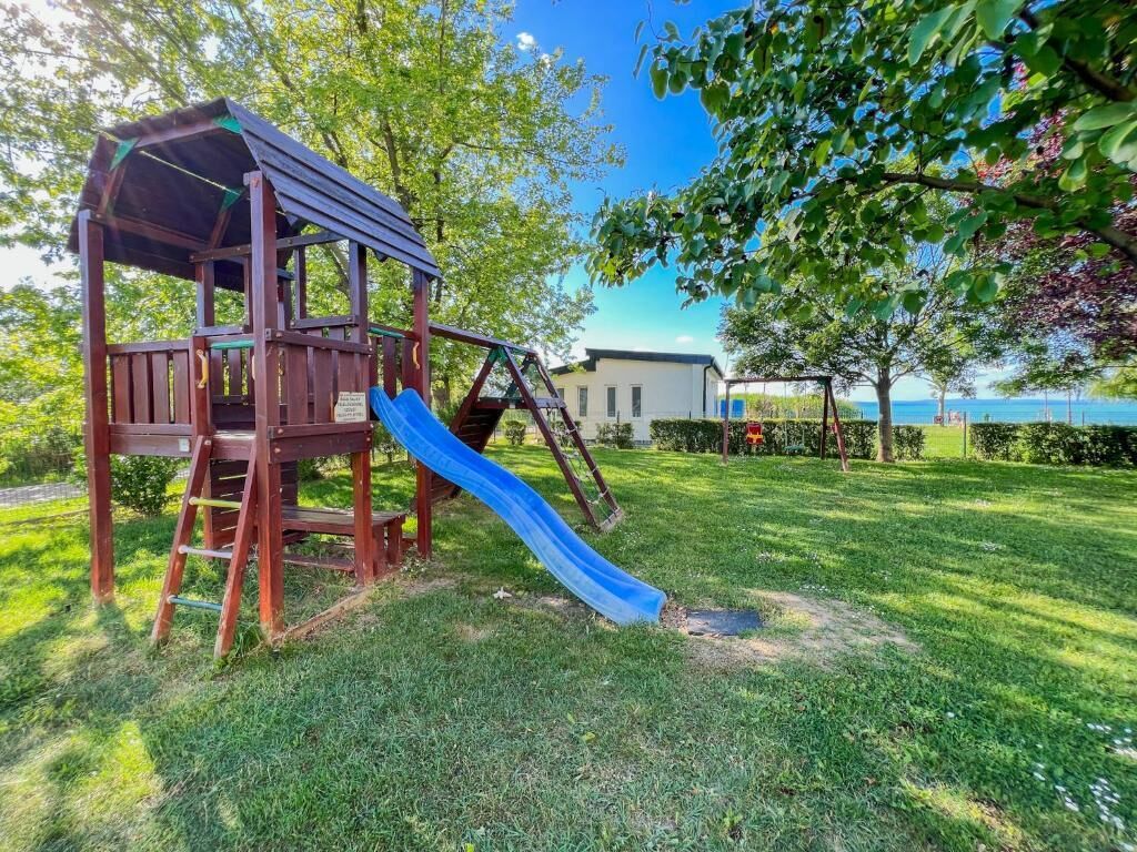 Une aire de jeux avec un toboggan et une structure d’escalade, entourée d’herbe et d’arbres.