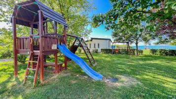 Une aire de jeux avec un toboggan et une structure d’escalade, entourée d’herbe et d’arbres.