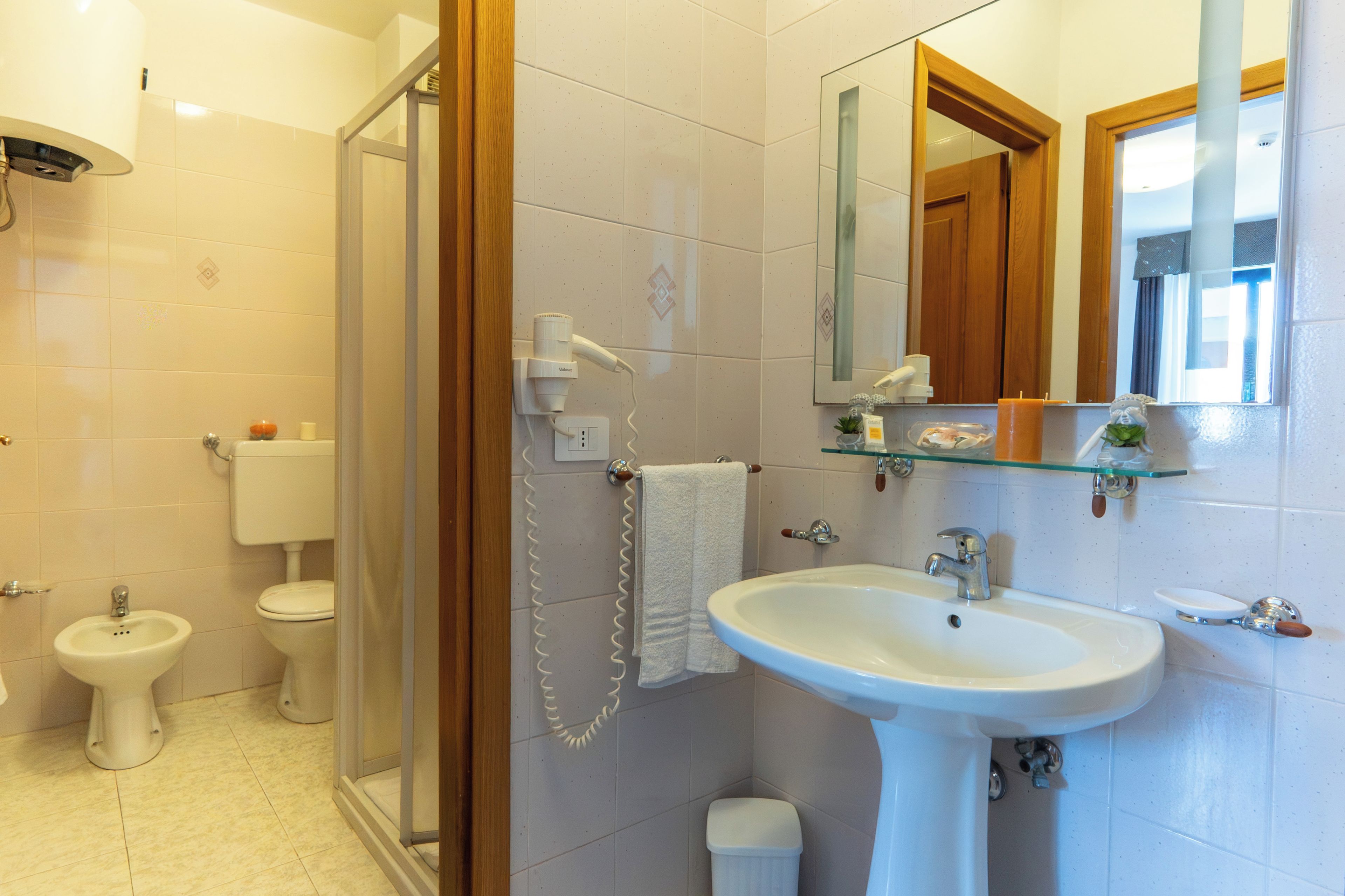 A bathroom with a glass shower enclosure, a pedestal sink, a toilet, and a bidet.